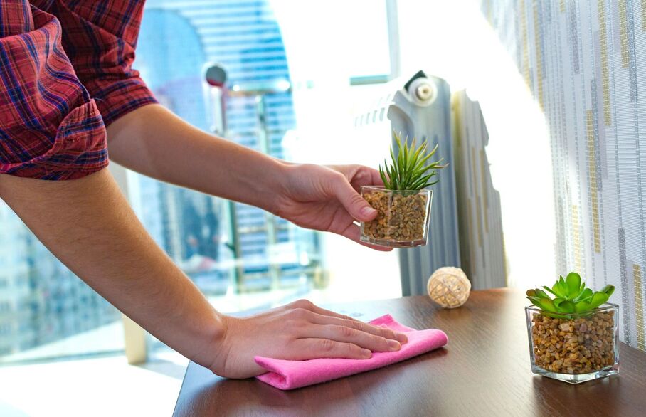 Someone lifting up a plant and wiping down a surface