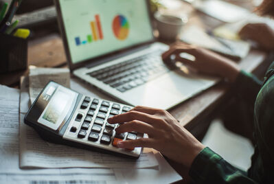 Someone holding a calculator over a contract with a small house in the background
