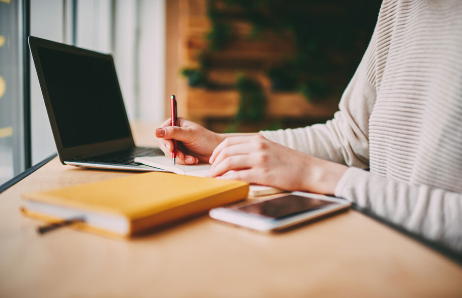 Someone writing in a notebook and typing on a computer