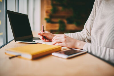 Someone writing in a notebook and typing on a computer