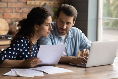 Two people sitting in front of a laptop looking at paper