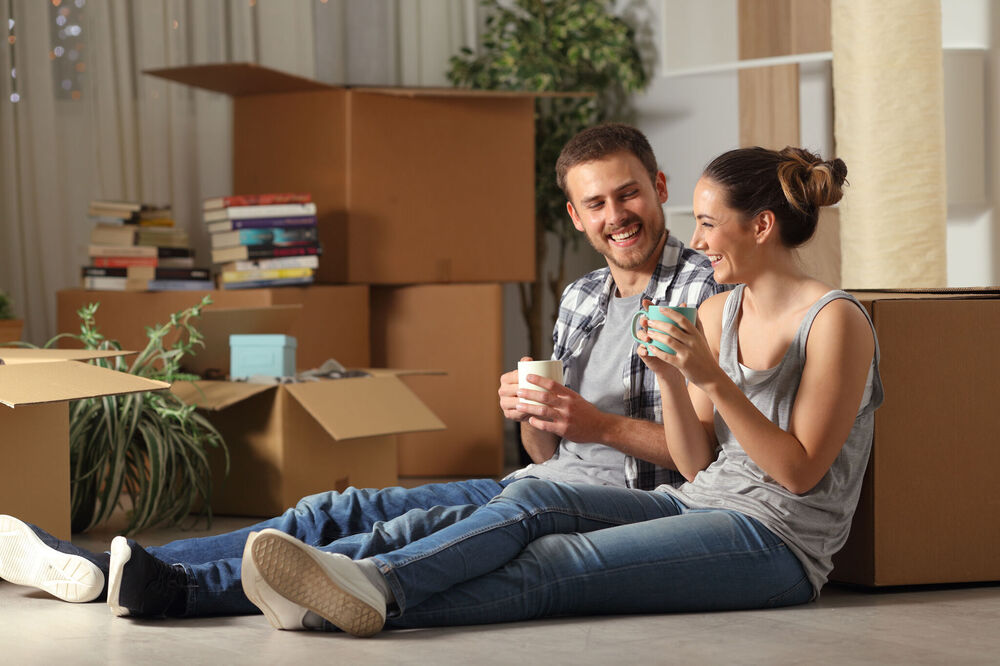 Happy couple sitting on floor surrounded by packing boxes