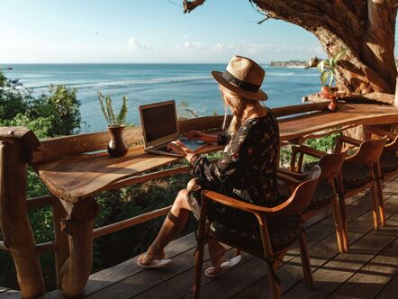 A person sitting in front of a laptop on a beachfront balcony