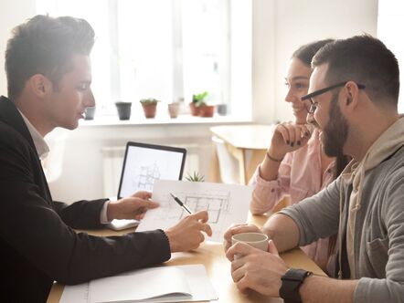 Two people having a meeting with a person holding house schematics