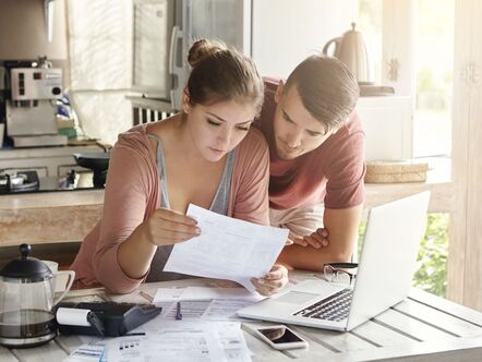 Two people looking at a piece of paper in front of a laptop